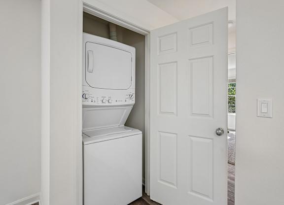 A white washing machine is in a small alcove in a white room.