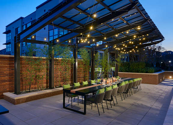 A patio with a long table and chairs under a roof with lights.