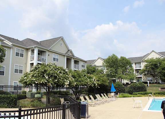 A swimming pool is surrounded by lounge chairs and trees in front of apartment buildings.