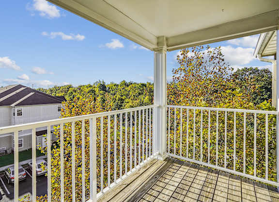 A balcony with a white railing overlooks a parking lot and a building.