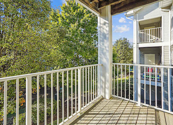 A balcony with a white railing and a view of a tree and a house.