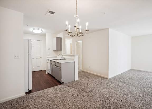 A kitchen with a sink and a refrigerator is in the middle of a room with a carpet on the floor.