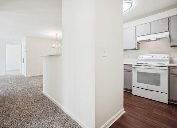 A kitchen with white appliances and a grey carpet.