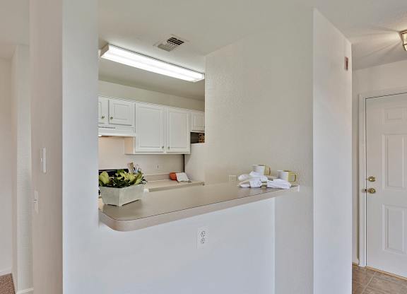 A kitchen with white cabinets and a countertop with a bowl of fruit on it.
