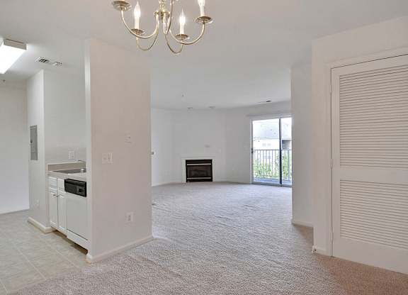 A large, empty living room with a chandelier and a kitchen area in the background.