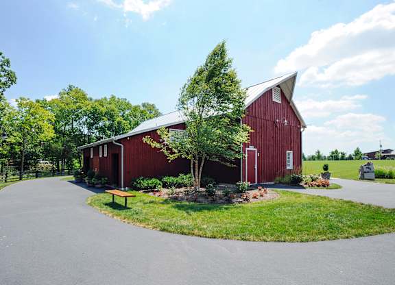 A red barn with a white door and windows is surrounded by a green lawn and trees.