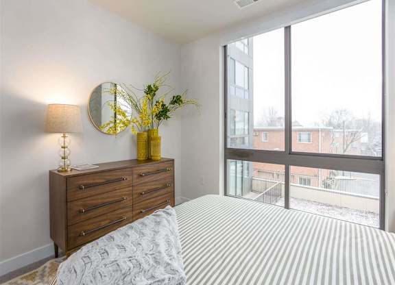 A bedroom with a bed, dresser, and a window overlooking a building.