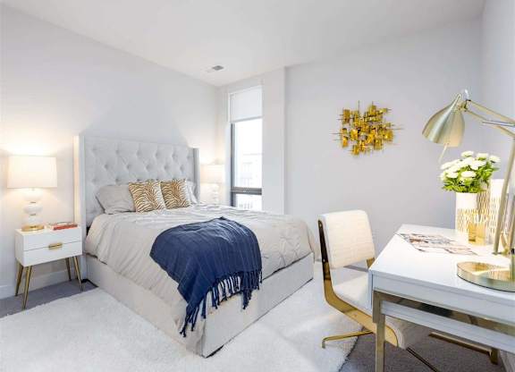 A bedroom with a large bed, a desk with a lamp, and a chair.