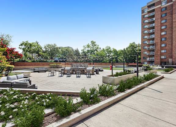 A large outdoor seating area with a concrete floor and a grassy area with a bench and a tree.