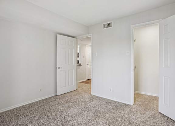A room with carpeted floor and three white doors.