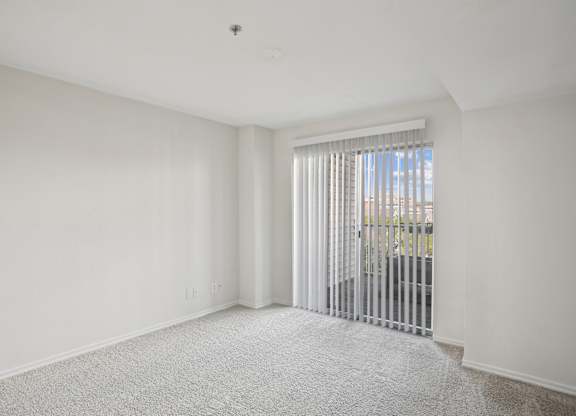 A white room with a carpeted floor and a window with blinds.