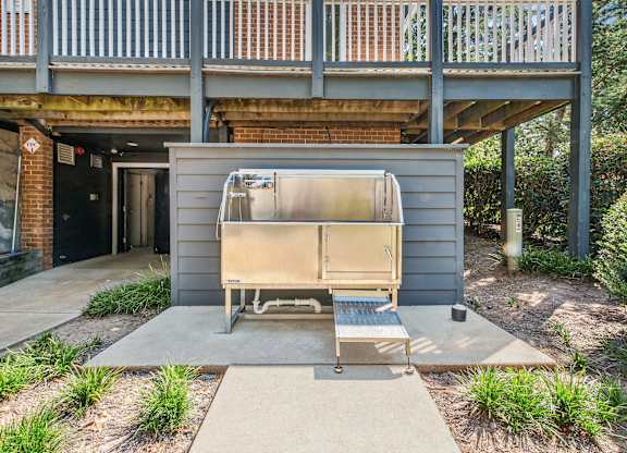 A small grey building with a door open and a bench in front.