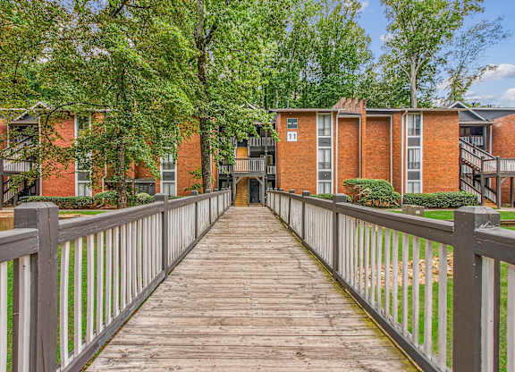 A wooden walkway leads to a brick building with a white fence on either side.