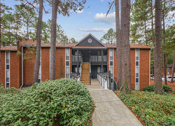 A building with a black roof and a small porch is surrounded by trees.
