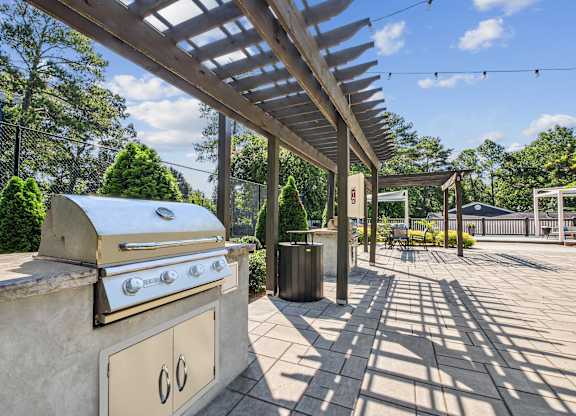 A BBQ grill is on a patio with a canopy over it.