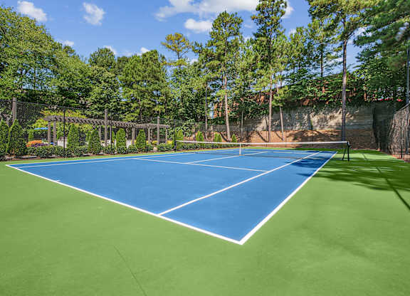 A tennis court surrounded by trees and a fence.
