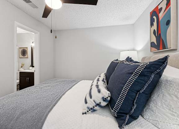 A bed with a grey blanket and a blue and white pillow.