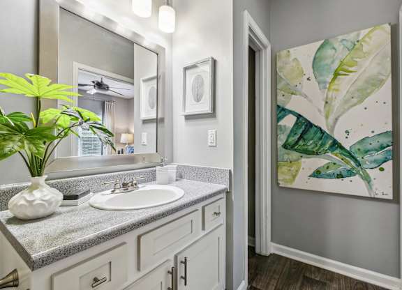 A bathroom with a sink, mirror, and a painting of a leafy plant.
