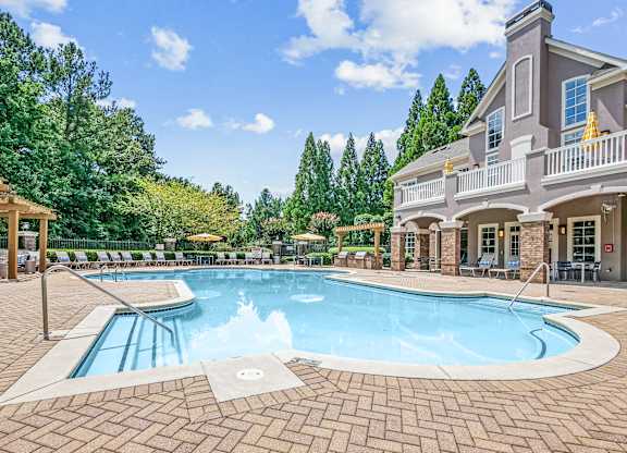 A large outdoor swimming pool surrounded by a brick patio and a house.