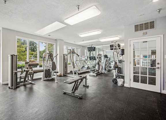 A spacious gym with a variety of equipment and a view of the outdoors through the windows.