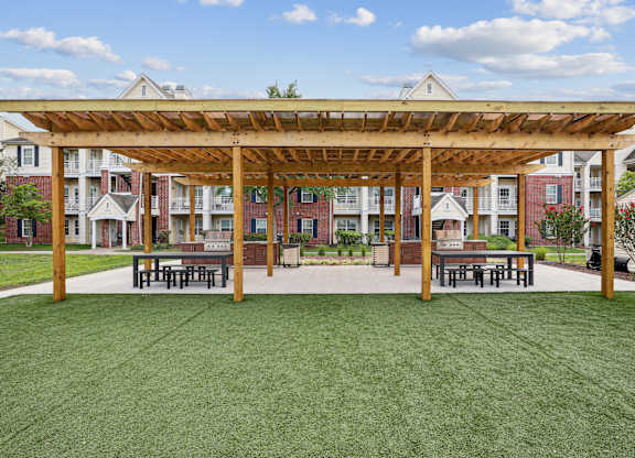 A wooden pergola is over a picnic table in a grassy area.