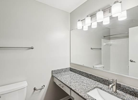A bathroom with a toilet, sink, mirror, and lighting fixture at Elme Manassas, Manassas, 20109