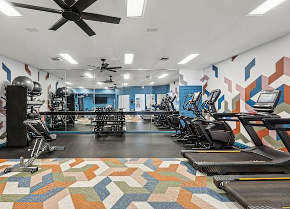 A gym with a variety of equipment including treadmills, elliptical machines, and a fan.