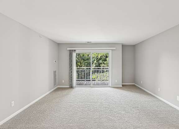 A spacious room with a carpeted floor and a sliding glass door leading to a balcony.