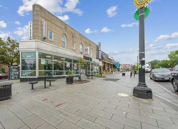 A street view with a building on the left and a pole with a flower on top on the right.