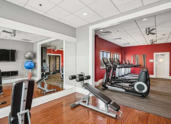 A gym with a variety of equipment including a weight bench, a television, and a mirror  at The Paramount, Arlington, Virginia