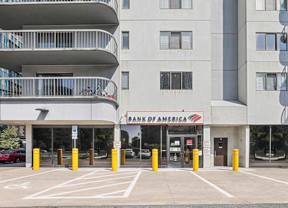 A Bank of America branch is located in a parking lot in front of a large apartment building.