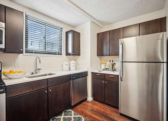 A kitchen with a refrigerator on the right and a sink with a bowl of fruit on the counter at Riverside Apartments, Alexandria, Virginia