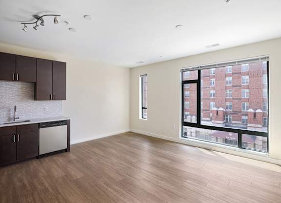 A large empty room with a kitchen area and a window overlooking a building at The Maxwell Apartments, Arlington