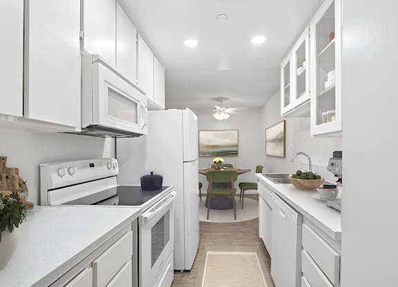 Kitchen 1005 Via Zapata apartment home with wood-style plank flooring, white cabinetry, white appliances and dining nook with overhead ceiling fan.
