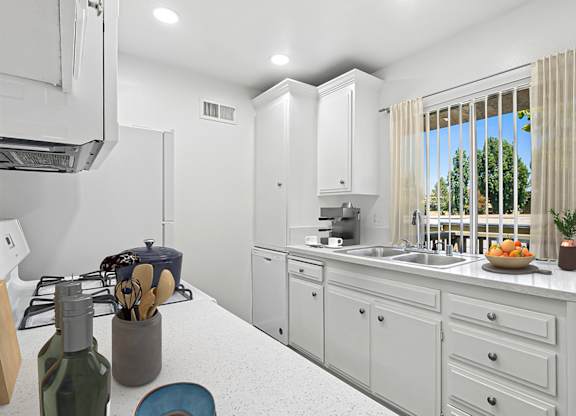Kitchen in 955 Via Zapata apartment home with wood-style plank flooring, white cabinetry, white appliances, and a view of the stunning trees throughout the community.