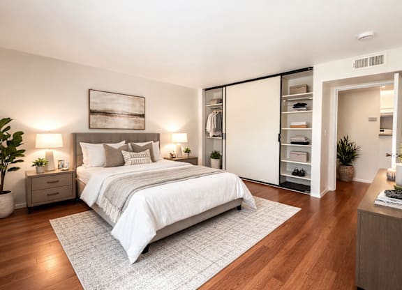 A bedroom with a large bed, a nightstand with a lamp, and a plant on the side table.