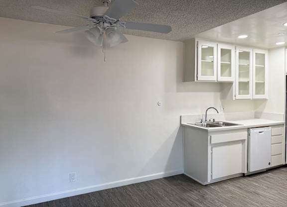 Kitchen in 1005 Via Zapata apartment home with wood-style plank flooring, white cabinetry, white appliances and dining nook with overhead ceiling fan.