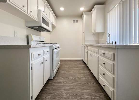 Kitchen in 955 Via Zapata apartment home with wood-style plank flooring, white cabinetry, white appliances, and a view of the stunning trees throughout the community.