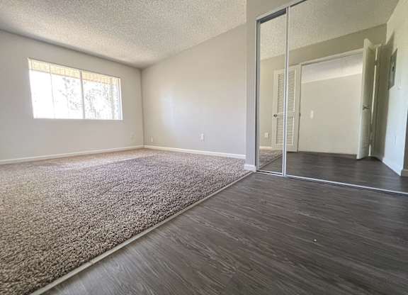 Oversized bedroom in 955 Via Zapata apartment home. Entryway inside the bedroom has wood-style plank flooring, a large closet with mirrors and a hallway on the right leading to a private vanity area and private bathroom.  Left side of room has plush carpeted flooring and large windows allowing for gorgeous natural lighting.
