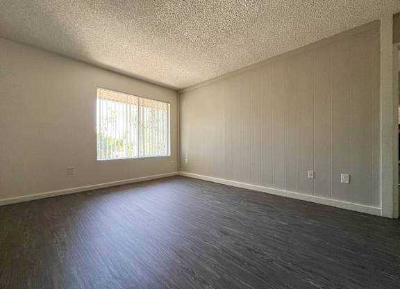 Spacious and charming living area in 955 Via Zapata apartment home with wood-style plank flooring, large windows and decorative wood paneled accent wall painted a light taupe/gray.