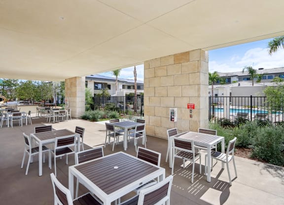 a patio with tables and chairs and a pool in the background at The Max on Jefferson Apartments, California