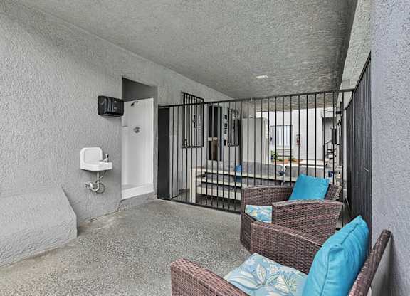A patio with a wicker chair and a cushion with a blue pillow and a white wall.