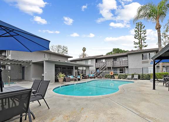A pool area with a blue umbrella and chairs.