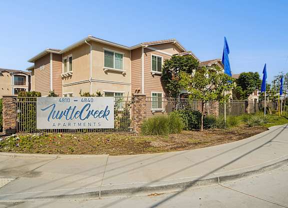 Turtle Creek Exterior with lush lined planters, a cool and modern monument and a charming building exterior