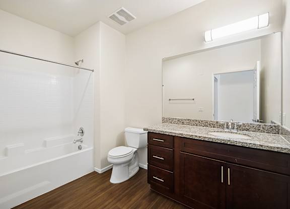 luxurious bathroom in Turtle Creek apartment home with wood-style plank flooring, modern dark wood cabinetry, modern fixtures, large vanity mirror and a shower/tub