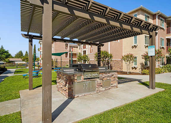 BBQ grilling station under shaded trellis at Turtle Creek surrounded by lush grass and park-like landscaping