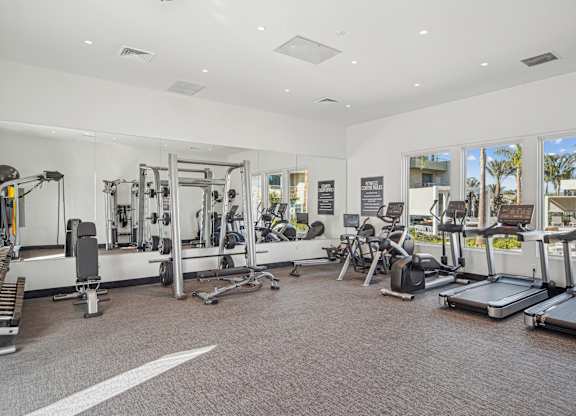 A spacious gym with a variety of equipment including treadmills, weights, and exercise machines at The Max on Jefferson Apartments, California, 92562