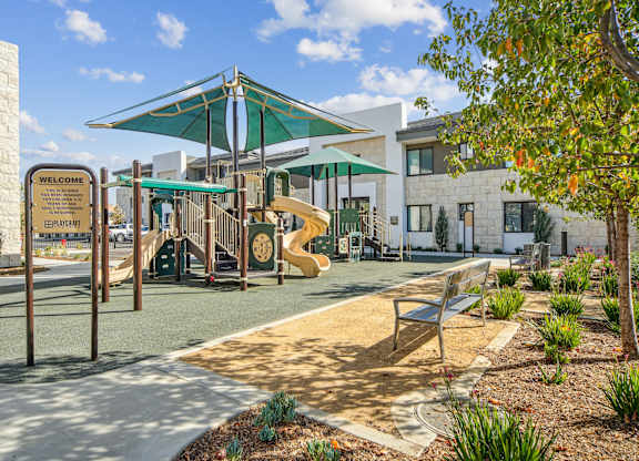 A playground with a slide, a bench and a tree at The Max on Jefferson Apartments, Murrieta, CA, 92562