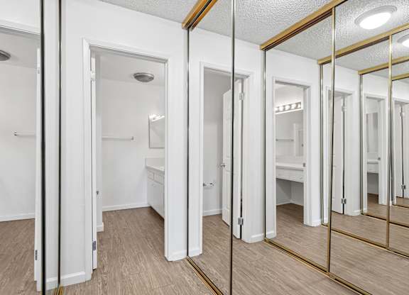 Hallway in primary bedroom leading to private bathroom lined with mirrored closet doors on both sides of the hallway
