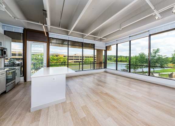 A kitchen with a white island in the middle of a room with wooden floors and a large window.